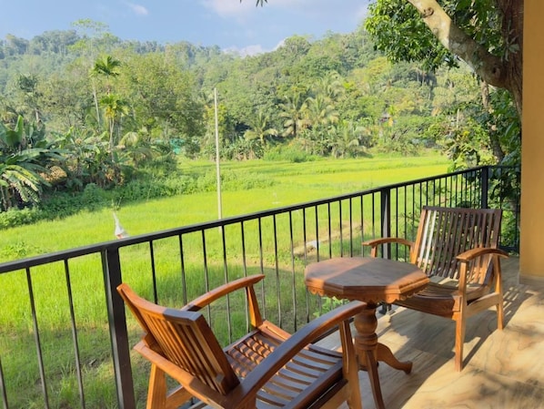 A balcony with wooden furniture overlooking a lush green landscape.