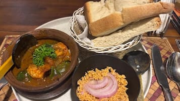 A plate with a stew, a bowl of rice, and a basket of bread.