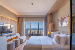 Une chambre d’hôtel comprenant un lit, une télévision, un balcon avec vue sur la mer et un coin repas.