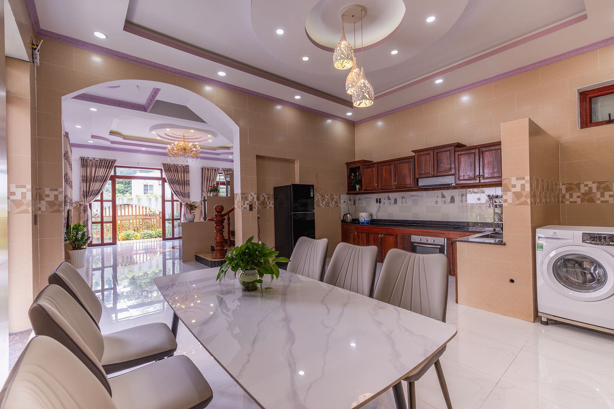 A modern kitchen with a dining area, featuring a marble table, wooden cabinets, and a built-in washing machine.