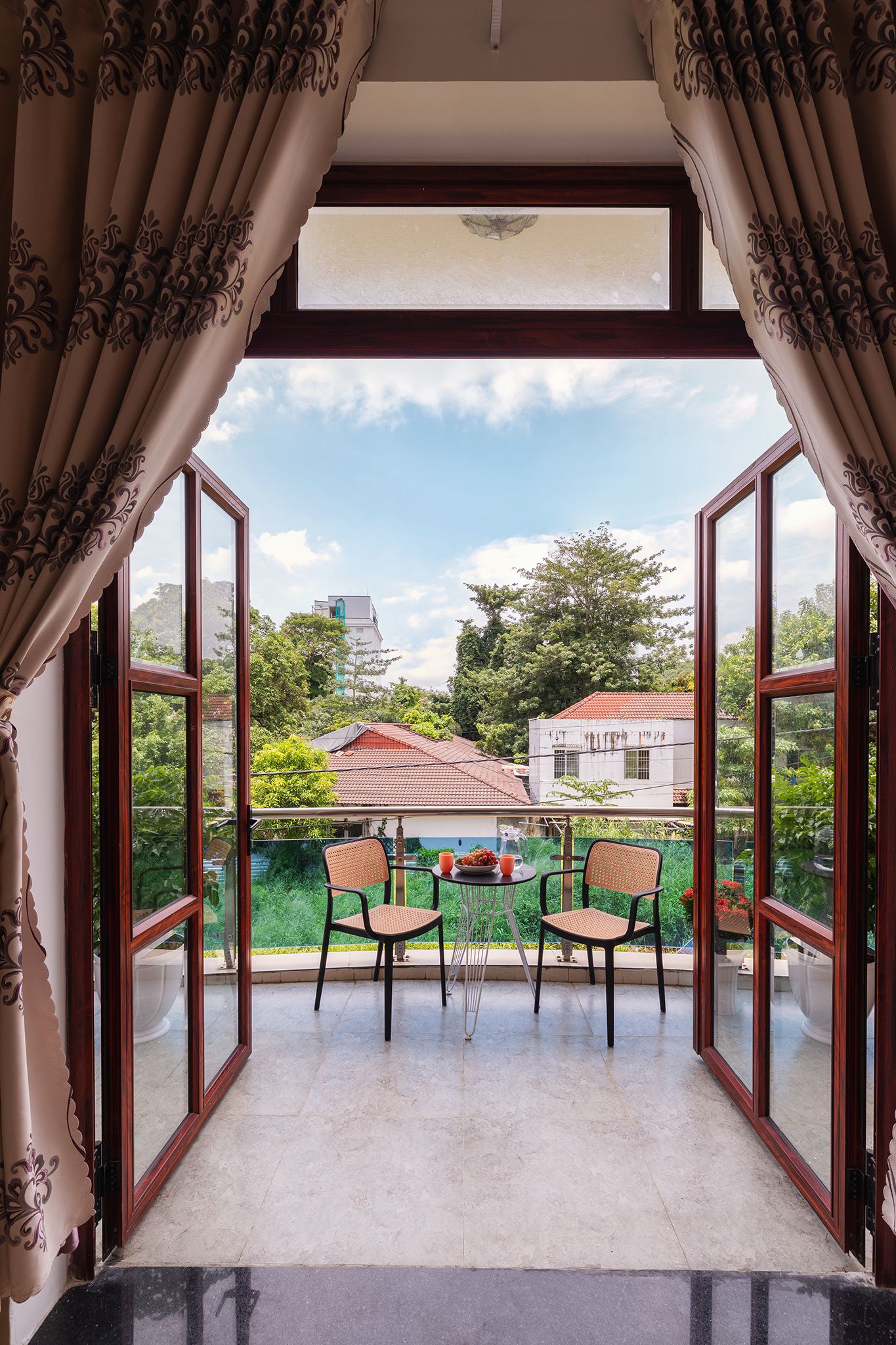 An open balcony with two chairs and a table, overlooking a residential area with trees and houses.