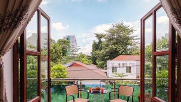 An open balcony with two chairs and a table, overlooking a residential area with trees and houses.