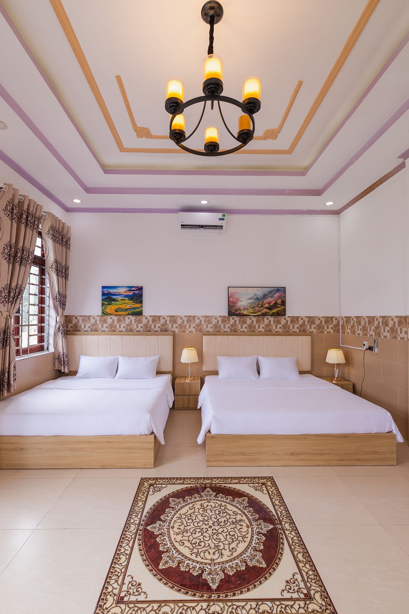 A hotel room with two beds, a chandelier, a large window with curtains, and a decorative rug.