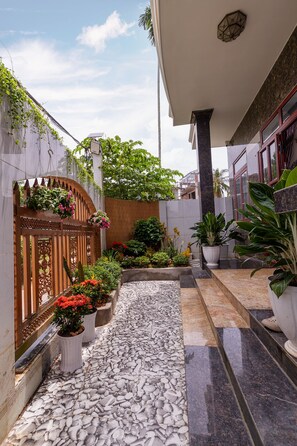 A courtyard with a tiled floor, potted plants, a wooden gate, and a building with a column. - Sunlit Seaside Villa Phú Quốc (Phú Quốc)