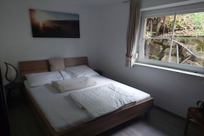 A bedroom with a bed, a window with curtains, a painting on the wall, and a chair. - Holiday home with a fantastic view (Hopfgarten im Brixental)