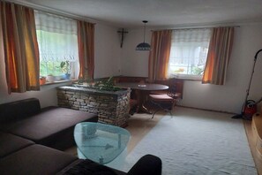A living room with a stone fireplace, a glass coffee table, a sofa, and a dining area with a table and chairs. - Holiday home with a fantastic view (Hopfgarten im Brixental)