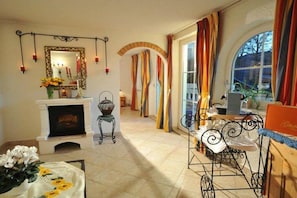 A room with a fireplace, a mirror, a table with flowers, and a view through large windows. - Holiday home with a fantastic view (Hopfgarten im Brixental)