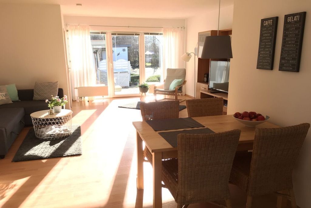 A living room with a sofa, a dining table with chairs, a TV, and a sliding glass door leading to an outdoor area.