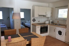 Cocina compacta con comedor, lavadora y cama en la habitación contigua.