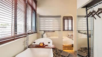 A modern bathroom with a freestanding bathtub, a sink, and a window with blinds.