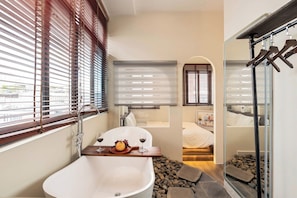 Une salle de bain moderne avec une baignoire sur pieds, un lavabo et une fenêtre équipée de stores.