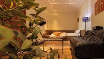 A modern living room with a sofa, a coffee table, and a lamp. There is a plant in the foreground.