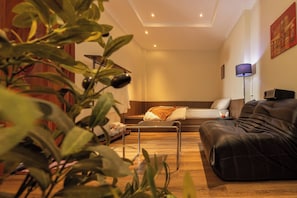 Un salon moderne avec un canapé, une table basse et une lampe. On aperçoit une plante au premier plan.