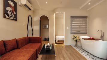 A modern hotel room with a sofa, a bathtub, and a wooden floor.