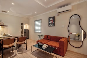 Un salon moderne comprenant un canapé, des fauteuils, une table basse, un coin cuisine et un grand miroir.