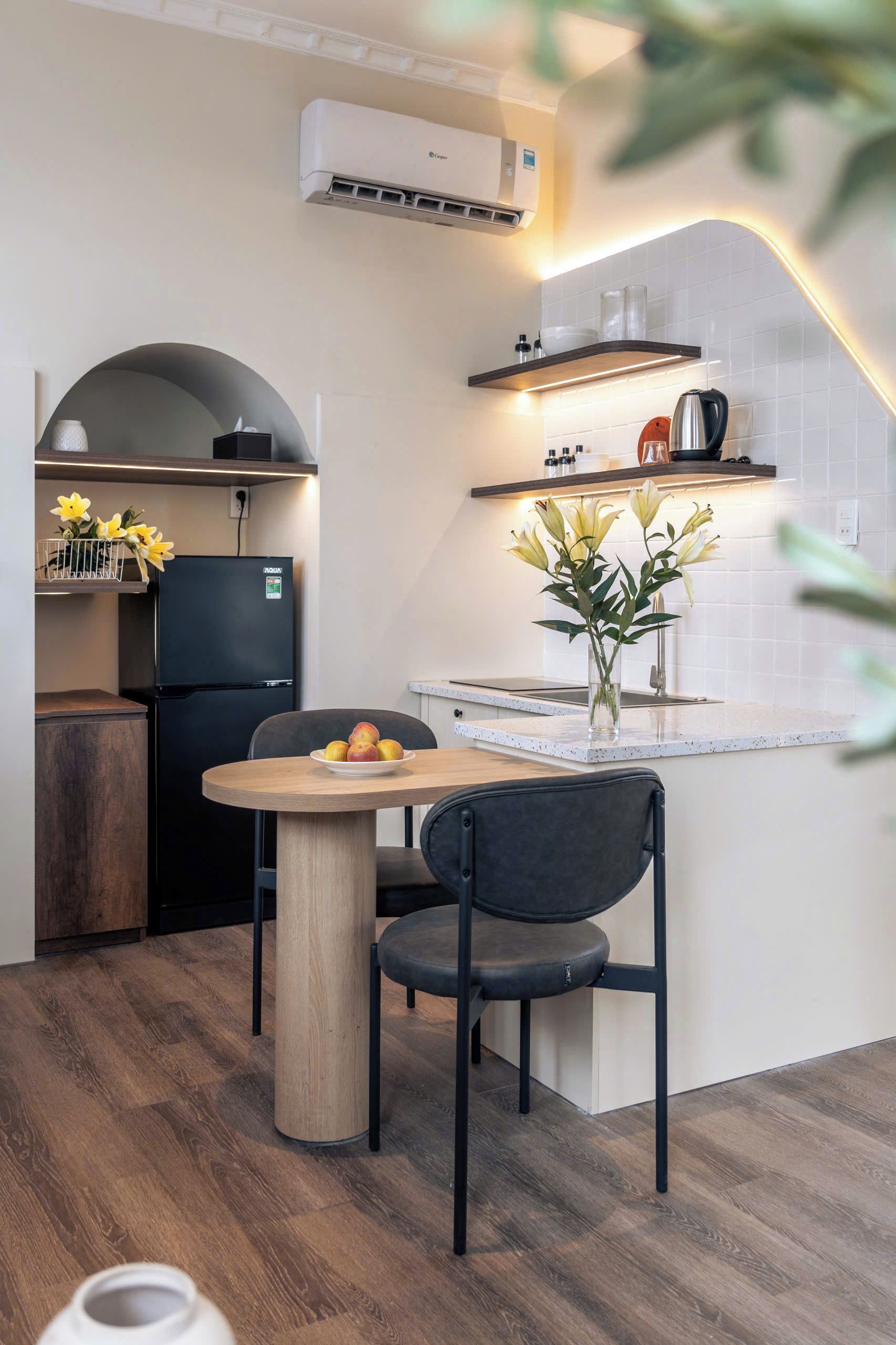 A modern kitchen with a built-in stove, a black refrigerator, and a dining area with a table and chairs.