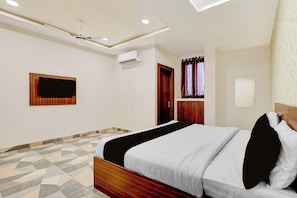 Een hotelkamer met een bed, een plafondventilator, een airconditioningapparaat, een televisie en een vloer met een patroon.