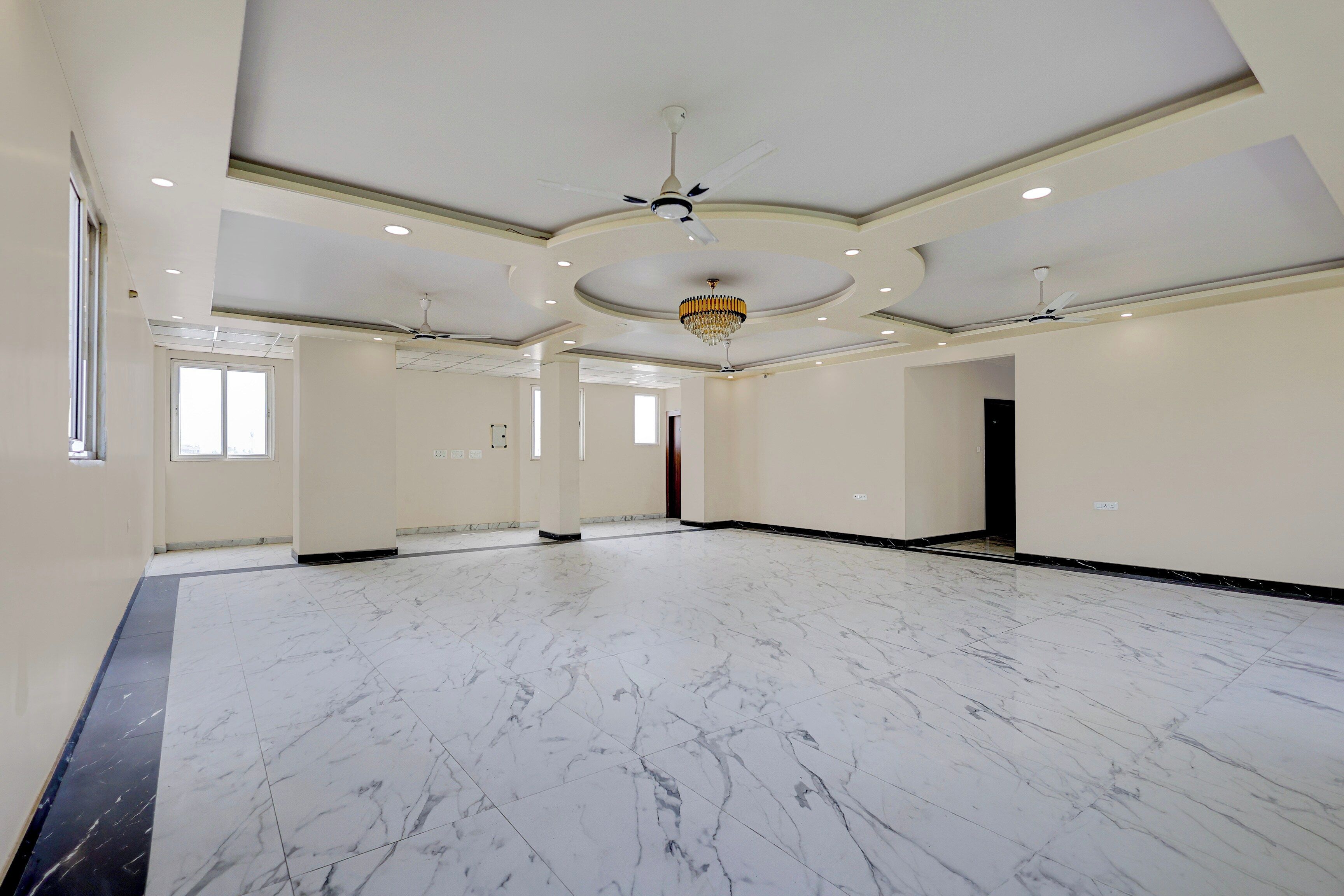 A spacious room with a marble floor, a chandelier, and ceiling fans.