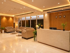 Un vestíbulo de hotel con mostrador de recepción, sofás y un reloj en la pared.