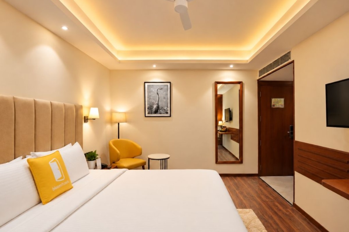 Habitación de hotel con cama, una silla, escritorio, espejo y televisor.