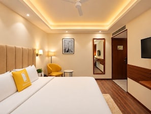 Habitación de hotel con cama, una silla, escritorio, espejo y televisor.