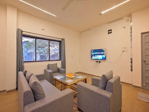 A room with a sofa set, a coffee table, a TV mounted on the wall, and a window with curtains. - Dancenter Hill View, Ooty (Ooty)