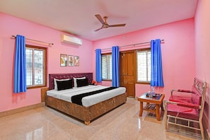 A bedroom with a bed, a ceiling fan, a window with curtains, a door, and a small table with a chair. - Dancenter Hill View, Ooty (Ooty)