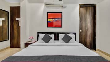 A hotel room with a bed, a nightstand, a vase of flowers, a painting, and an air conditioning unit.