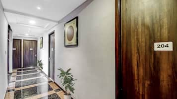 A hotel corridor with a checkered floor, wooden doors, and numbered room signs.