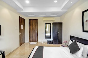 A hotel room with a bed, a nightstand, a mirror, a wardrobe, and an air conditioning unit. - Super Townhouse All In One (Kolkata)