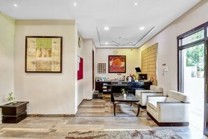 Een hotellobby met een receptiebalie, zithoek, kunstwerken en uitzicht door een groot raam.