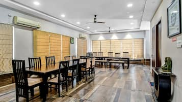 A conference room with multiple tables and chairs, ceiling fans, and air conditioning units.