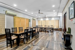 Un salón de conferencias con varias mesas y sillas, ventiladores de techo y unidades de aire acondicionado.