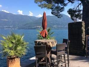 Un espace extérieur aménagé avec une table et des chaises, offrant une vue sur un plan d’eau et des montagnes.