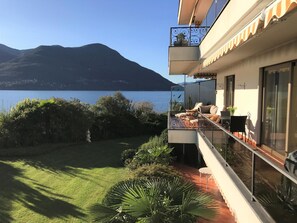 A balcony with a view of a lake and mountains, a grassy area, and a cactus plant. - La Palma by Interhome (Brissago)