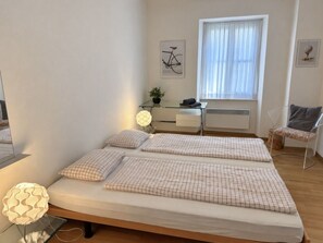 Ein Schlafzimmer mit einem Bett, Nachttischen, einem Schreibtisch, einem Stuhl und einem Fenster mit Vorhängen.