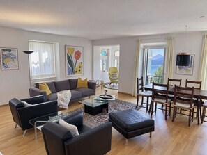 Ein modernes Wohnzimmer mit einer Couch, Sesseln, einem Couchtisch und einem Essbereich mit Tisch und Stühlen.
