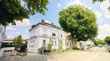 Ein historisches Gebäude mit einer traditionellen Fassade, einer Kopfsteinpflasterstraße und alten Bäumen.