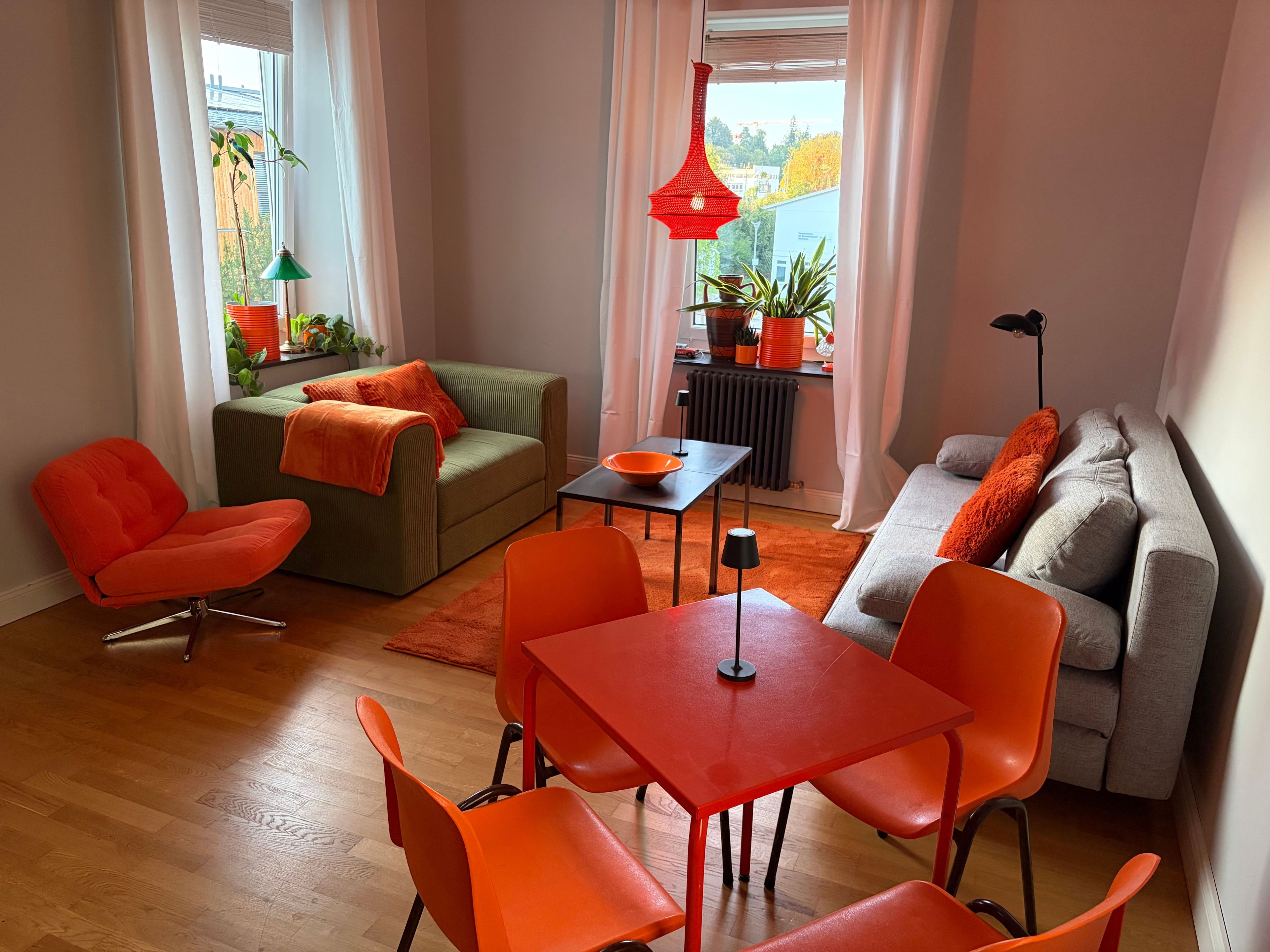 Ein modernes Wohnzimmer mit einem grünen Sofa, orangefarbenen Sesseln und einem grauen Sofa mit orangen Kissen.