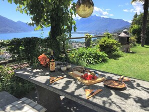 Un área de comedor al aire libre con una mesa de piedra, una botella de vino, una hogaza de pan, tomates y un pastel.