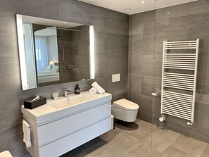 A modern bathroom with a large mirror, a white sink, a toilet, and a towel rack. - Residenza Lotus by Interhome (Minusio)