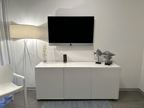 Quarto moderno com TV de tela plana presa a um armário branco, abajur, vaso com flores e escultura decorativa de peixe.