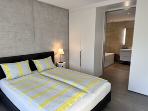 A modern bedroom with a large bed, a bedside lamp, and a view into a bathroom. - Residenza Lotus by Interhome (Minusio)