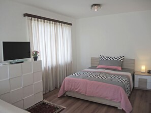 A bedroom with a bed, bedside table, TV, curtains, and a small plant. - Attico Luciana by Interhome (Minusio)