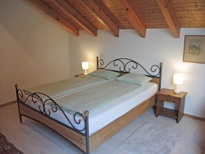 A single bed with a wooden frame and metal headboard, flanked by two bedside tables with lamps, in a room with wooden beams on the ceiling. - Casa Gialla by Interhome (Locarno Tegna)