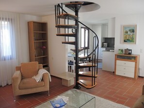 A living room with a spiral staircase, a sofa, a coffee table, and a kitchen area in the background. - Casa Gialla by Interhome (Locarno Tegna)