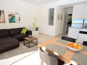 A modern living room with a sofa, coffee table, and dining area with a fruit bowl. - Collina d'Oro App. C14 by Interhome (Orselina)