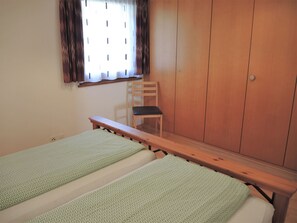 Ein Zimmer mit zwei Einzelbetten, einem Holzstuhl und einem Kleiderschrank.