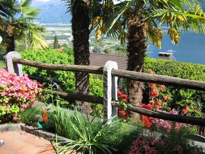 Ein Garten mit Holzzaun, üppigem Grün und Blick auf einen See sowie Berge im Hintergrund.
