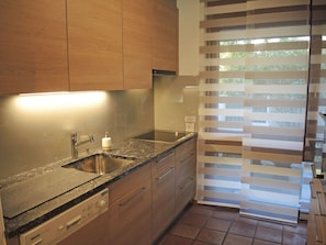 A modern kitchen with a granite countertop, stainless steel sink, and wooden cabinets. - Piccolo Mondo 1 by Interhome (Minusio)